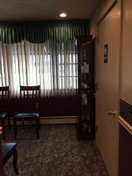 Open window with vertical blinds next to curio cabinet standing on the same wall as the door. Slat-back chairs are visible.