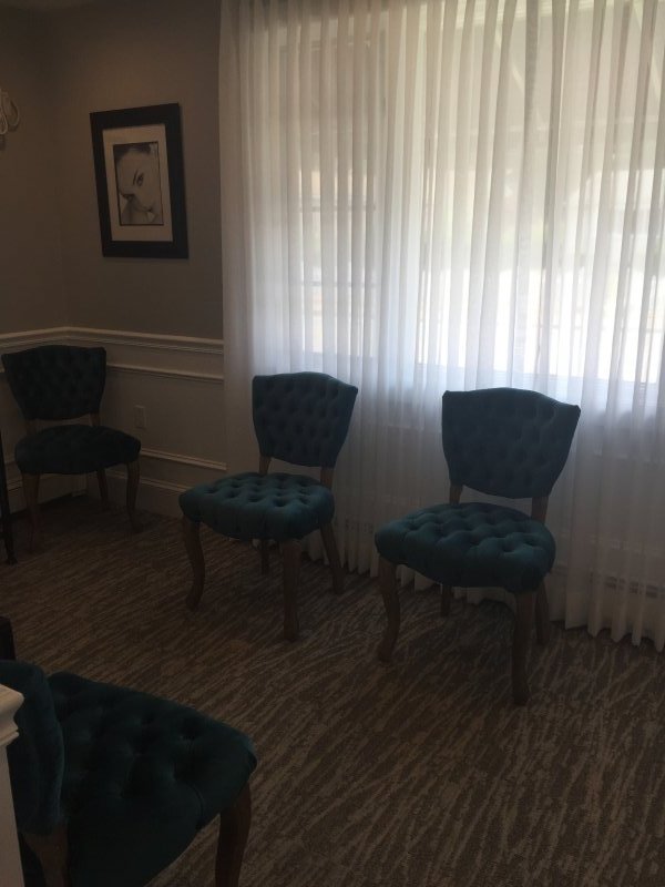 A newly rennovated waiting area with drape in front of vertical blinds and upholstered chairs.