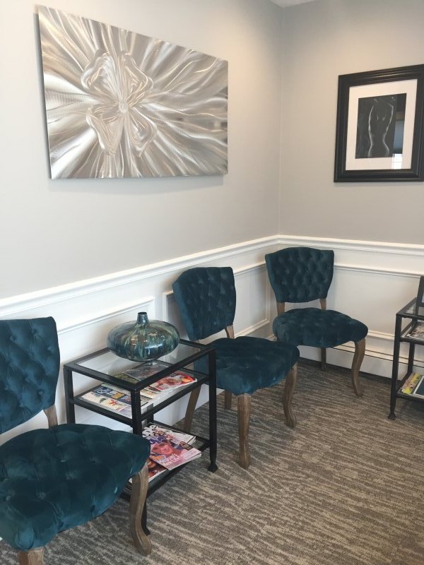 View of waiting room with new upholstered chairs, and side tables with decorative pieces underneath artwork on walls.