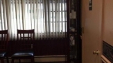 Open window with vertical blinds next to curio cabinet standing on the same wall as the door. Slat-back chairs are visible.