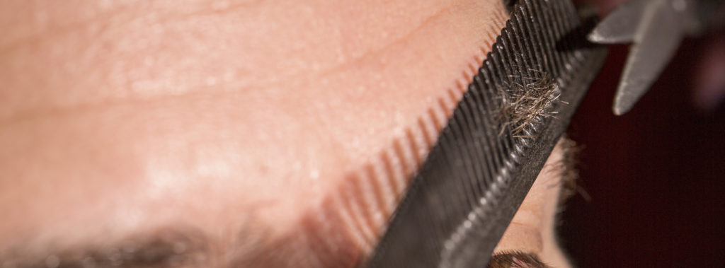 A pair of eyebrows being trimmed with a pair of scissors. and a comb as a guide. 