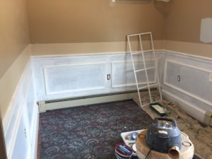 A completely bare room being prepped for decorative woodwork and shelving with a industrial vacuum and tools on the carpeted floor.