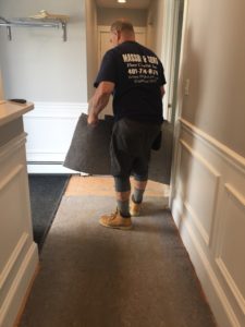 A man standing in a hallway with flooring in his hands, as he prepares to place it as part of renovations.