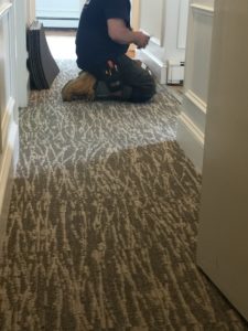 A man kneeling on newly installed flooring, as he prepares to anchor the flooring with a door plate. 