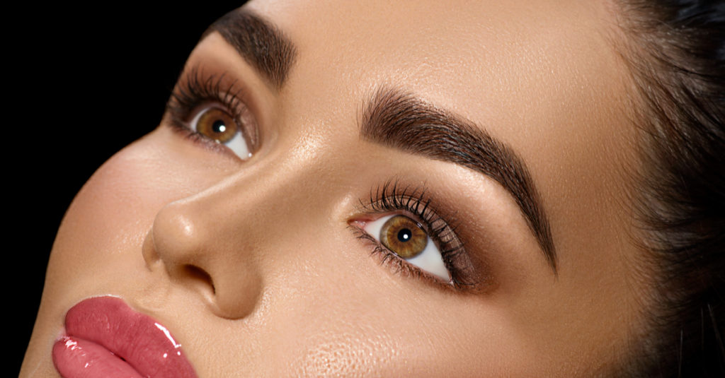 A close up view of shaped eyebrows on a womans face. The lines are sharp and crisp, and accented by eyeshadow and lashes.