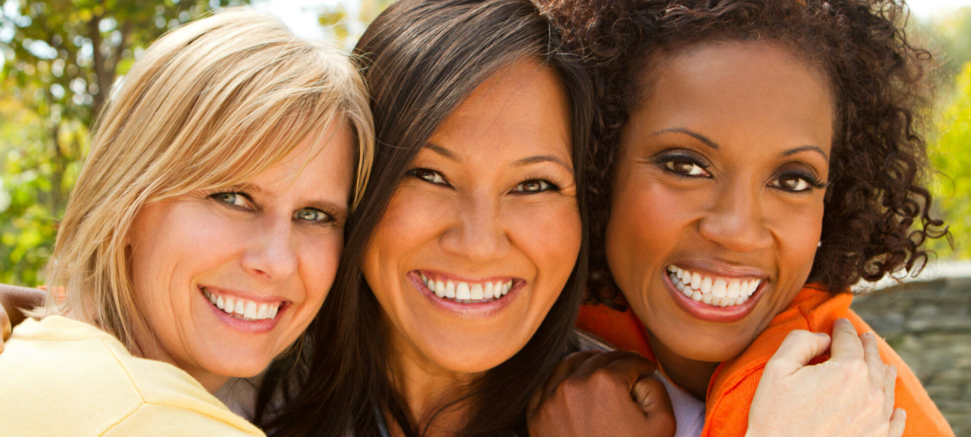 Three women smiling and showing bright white teeth to the camera.