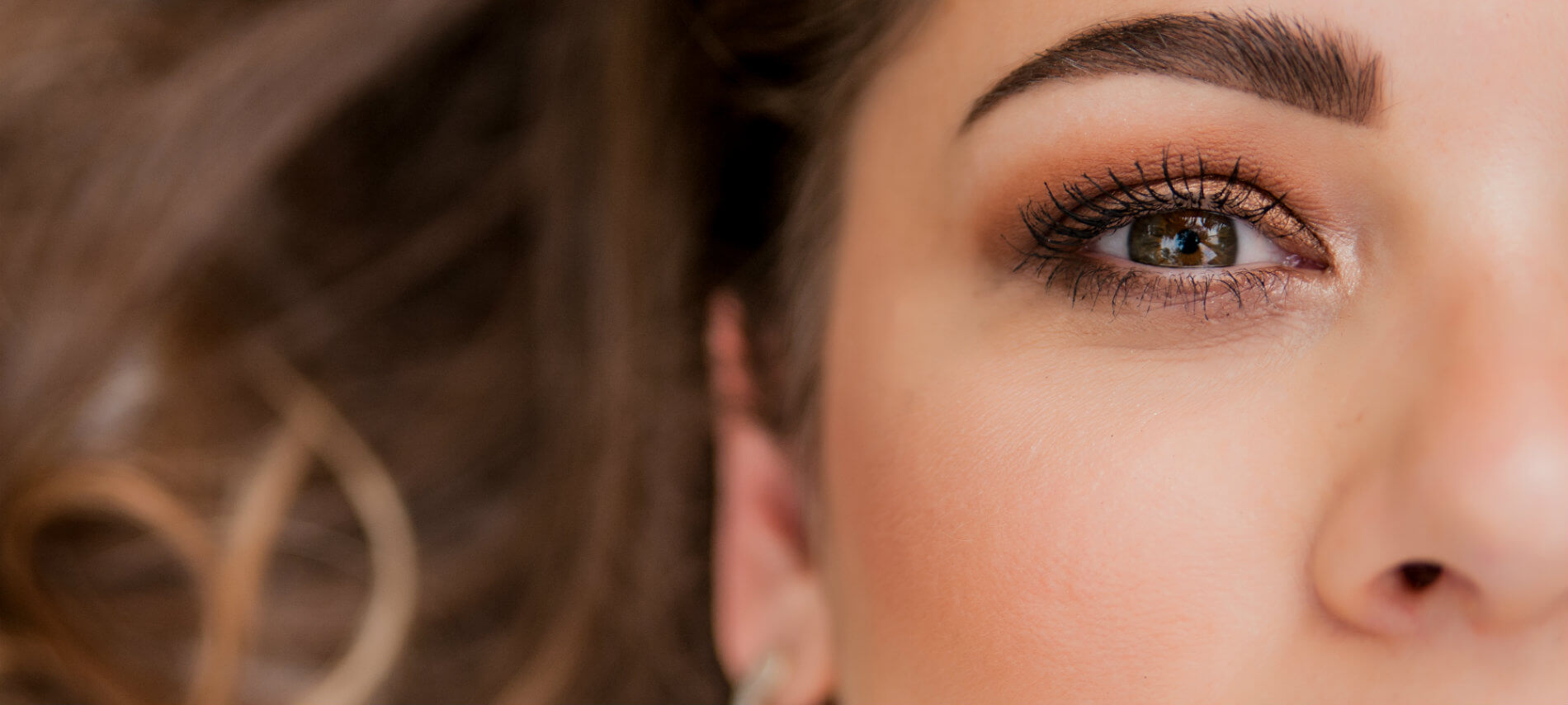 Close up view of a womans deep black eyelashes and against gracefully curved yet crisply sculpted eyebrows.