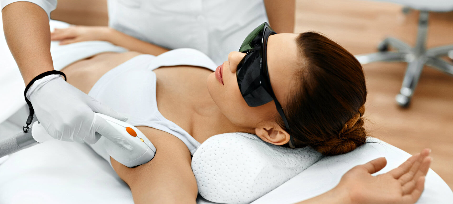 A woman in dark glasses receiving a hair treatment on her axila or armpit.